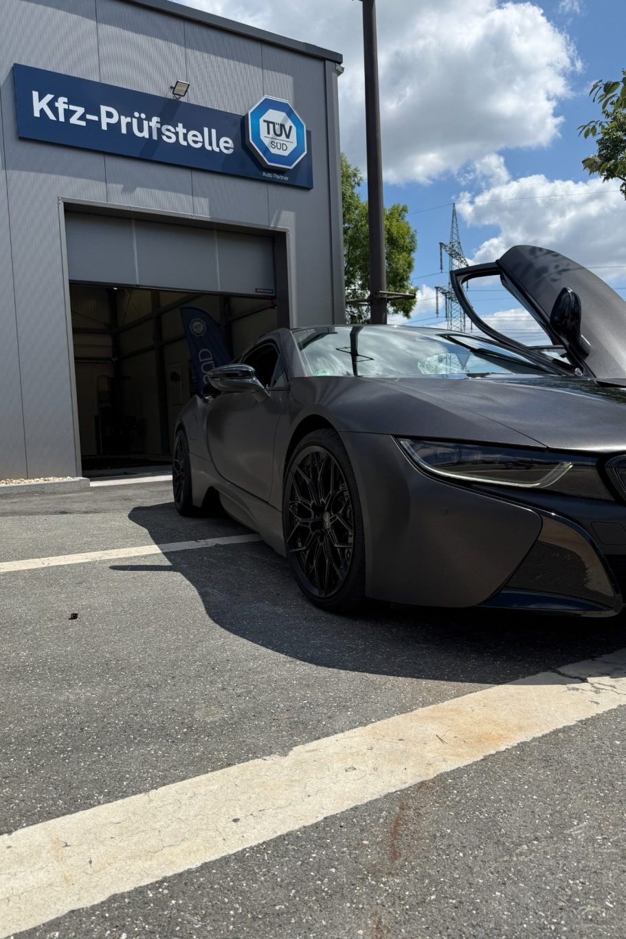 Schwarzer BMW I8 mit offener Tür vor der Einfahrt der KFZ-Prüfstelle